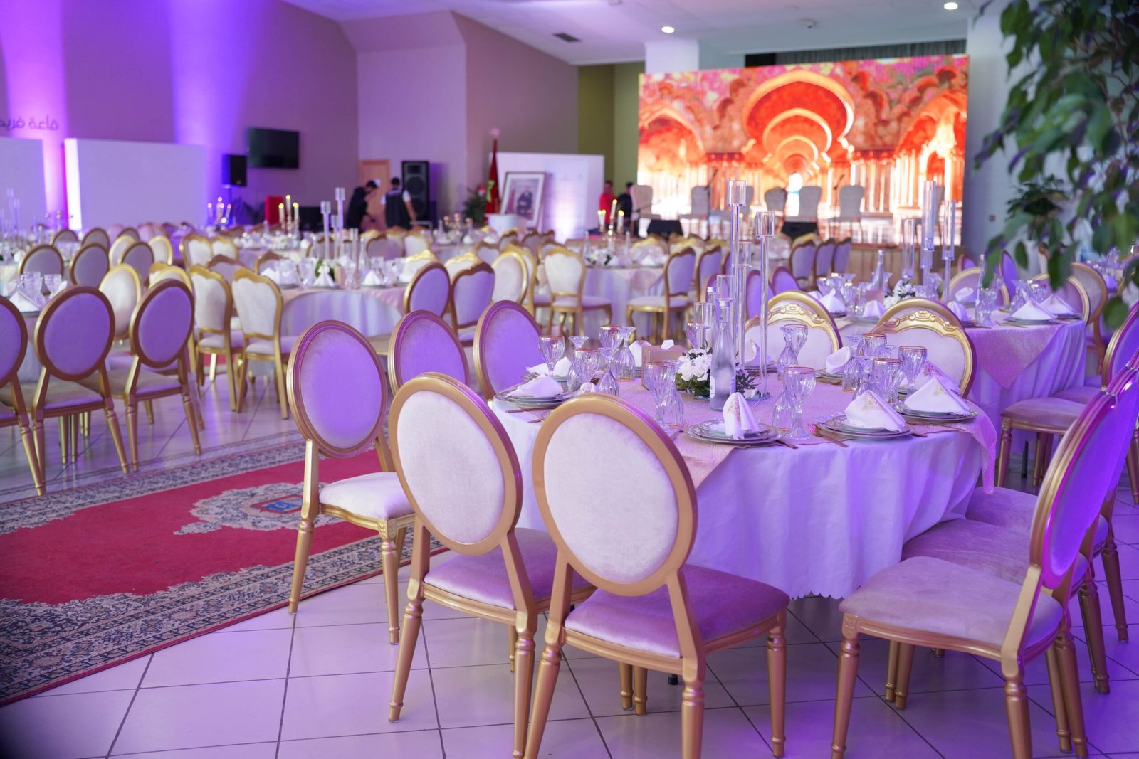 Luxurious banquet hall set for a grand event with elegant decor, purple lighting, and arranged tables.