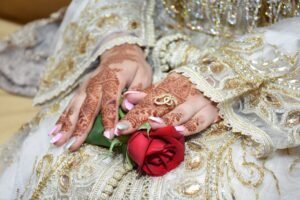 Bride's hands adorned with henna, holding a red rose, showcasing intricate cultural patterns.