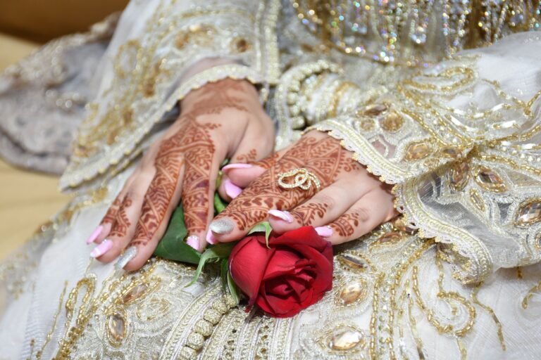 Bride's hands adorned with henna, holding a red rose, showcasing intricate cultural patterns.